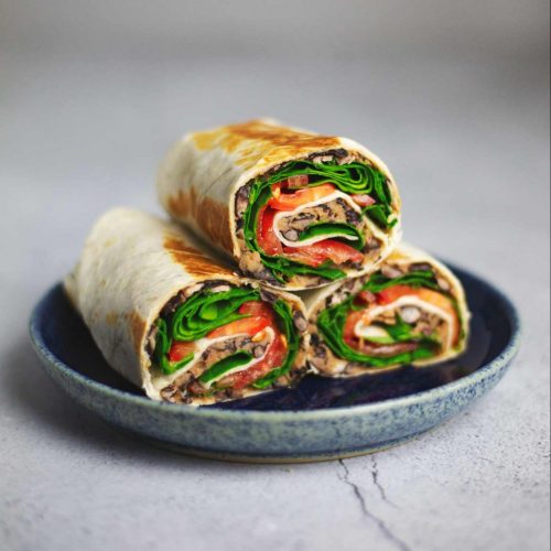 A tortilla wrap filled with black beans, cheese, spinach and tomato