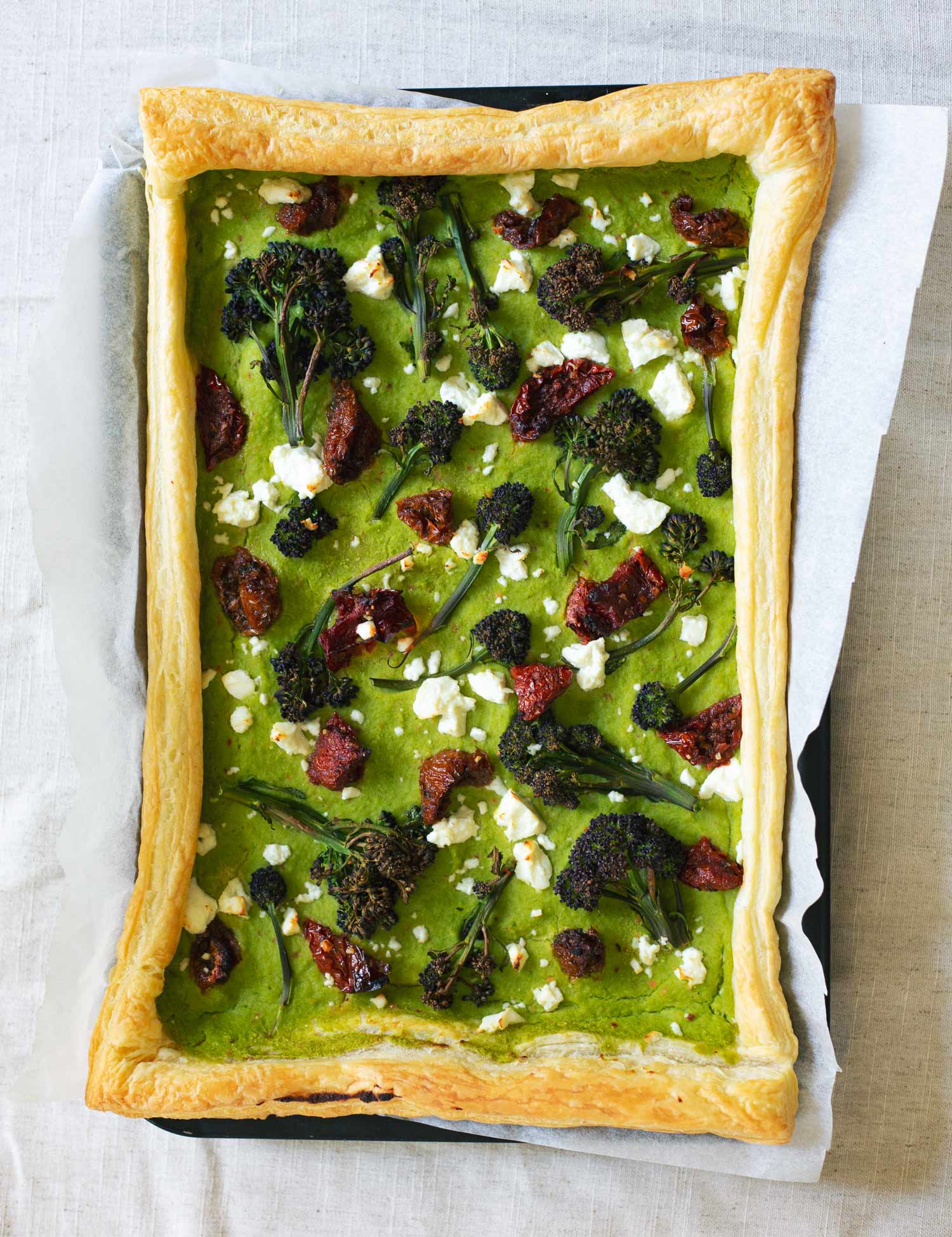 A tray with a rectangular tart topped with pea puree, broccoli, feta and sundried tomato