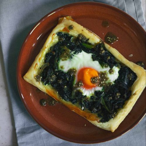 A pastry tart with greens and eggs on a red plate